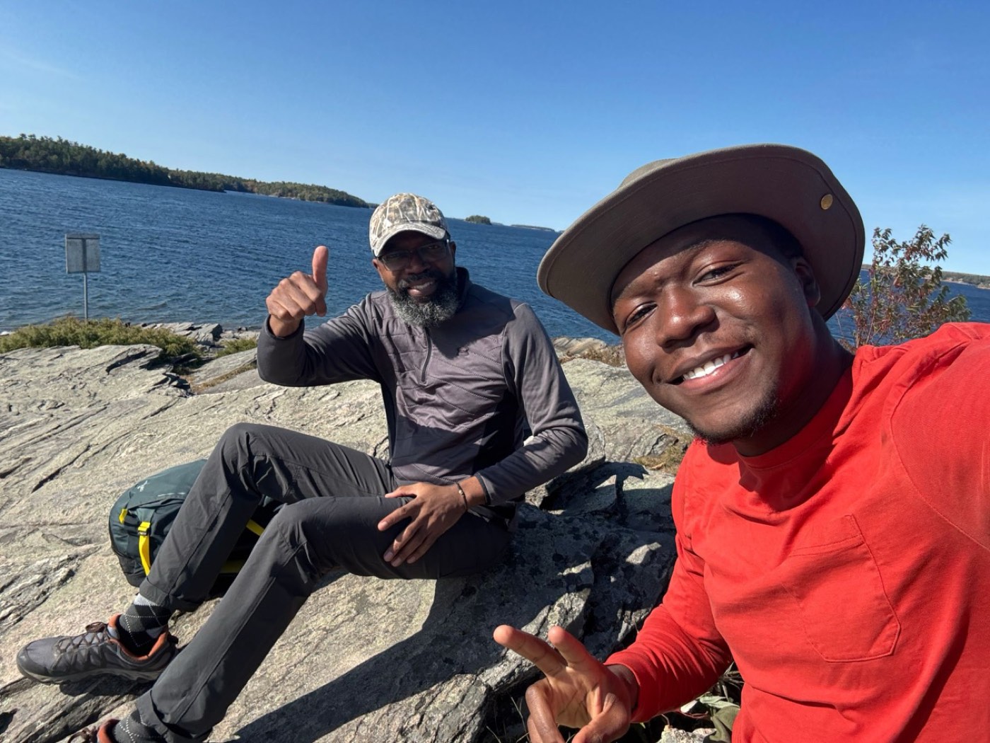 David and a hiking companion resting on lakeside rocks, smiling